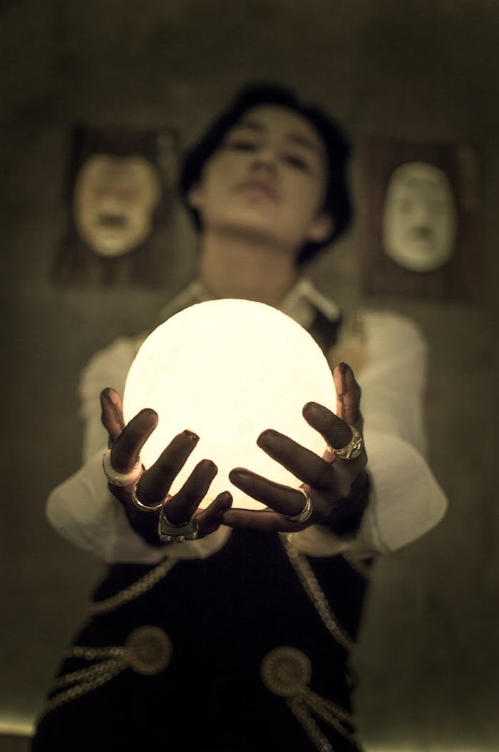 A mysterious figure holds an illuminated sphere in a dark, conceptual setting.